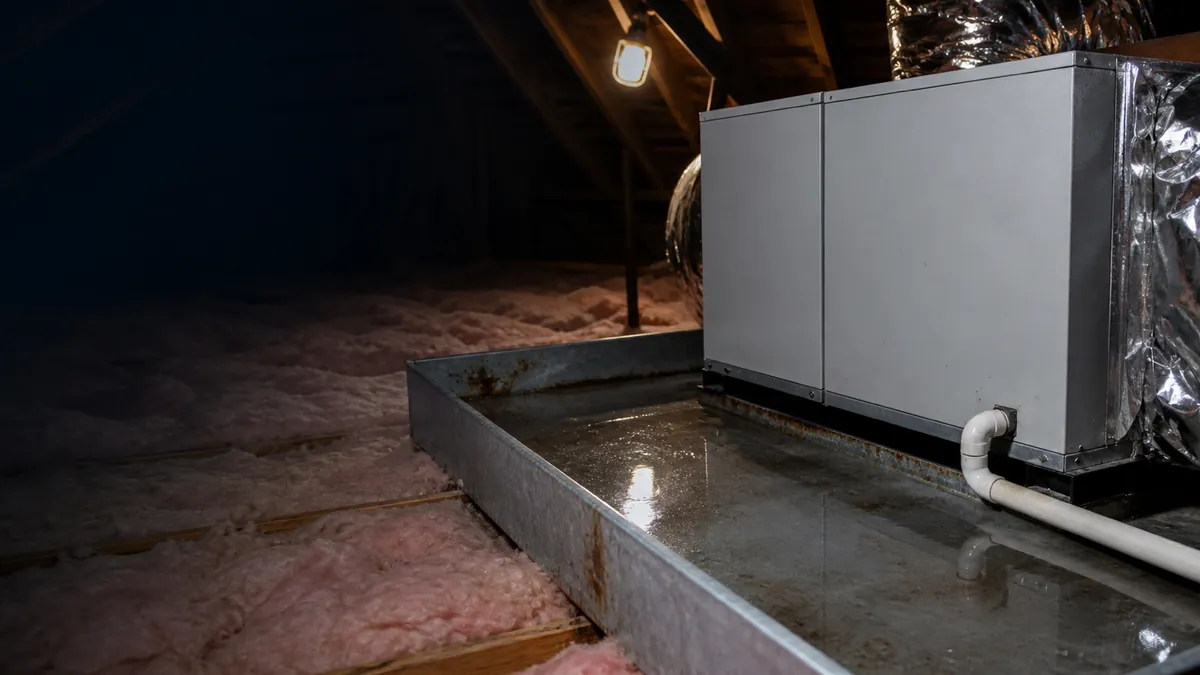 An attic air handler sitting in a drain pan full of standing water, with pink insulation around it.